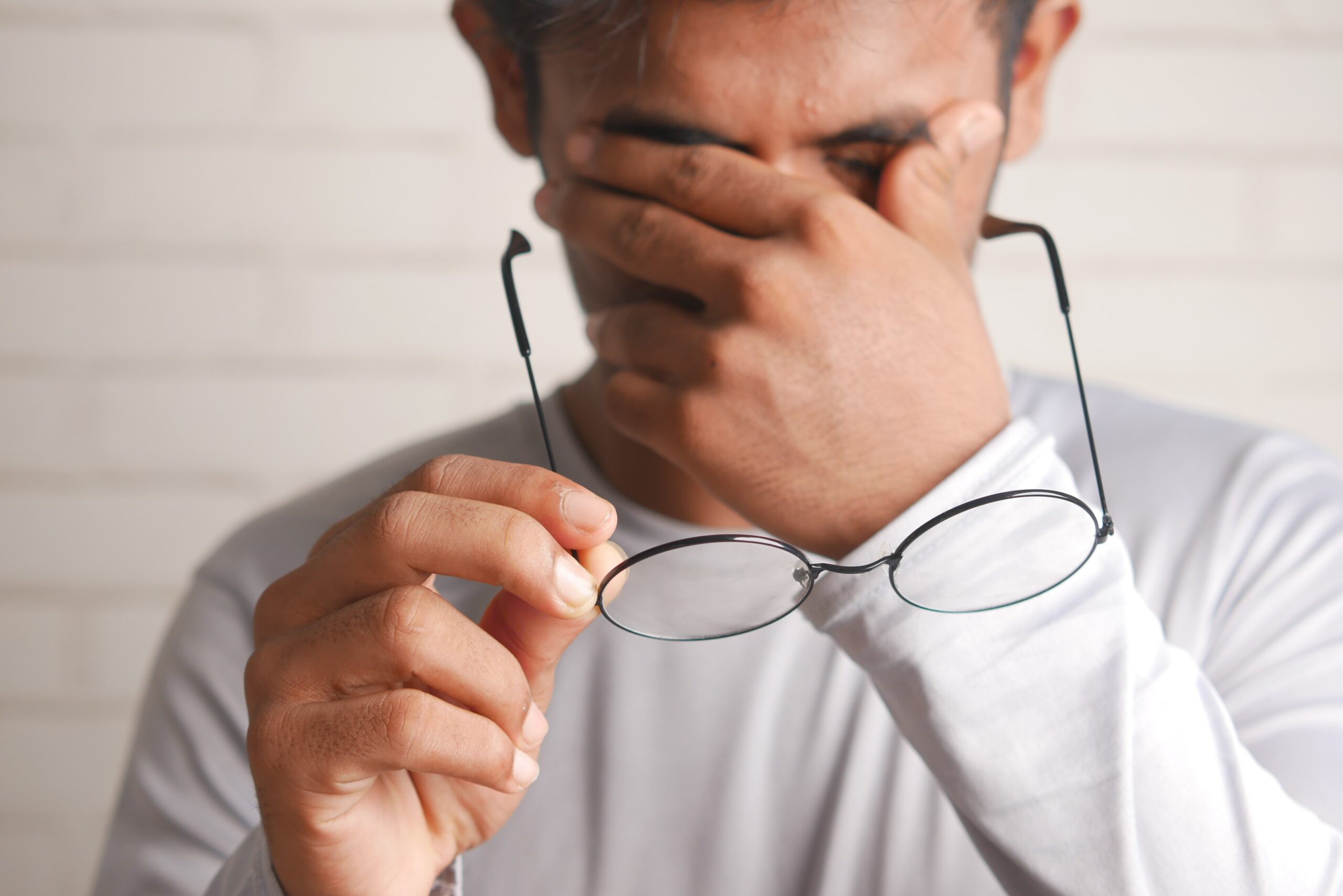 man rubbing his eyes and holding a pair of glasses